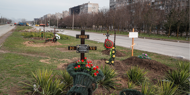 Graves of civilians killed during Ukraine-Russia conflict are seen next to apartment buildings in Mariupol on Sunday.