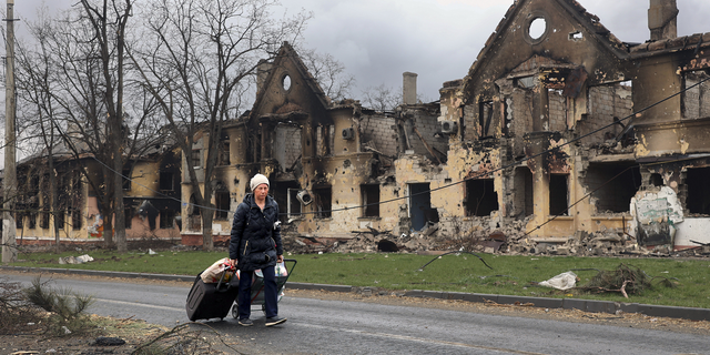 A woman on Friday pulls her bags past houses damaged during a fighting in Mariupol.