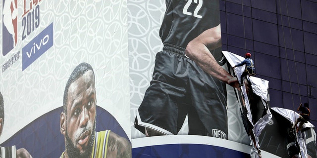 Workers pull down a banner advertising the Brooklyn Nets-Los Angeles Lakers game in Shanghai, China, on Oct. 9, 2019.