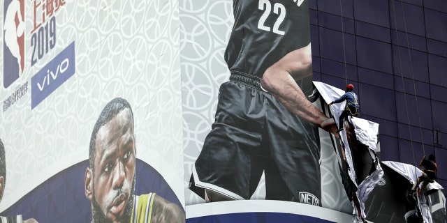 Workers pull down a banner advertising the Brooklyn Nets-Los Angeles Lakers game in Shanghai, China, on Oct. 9, 2019.