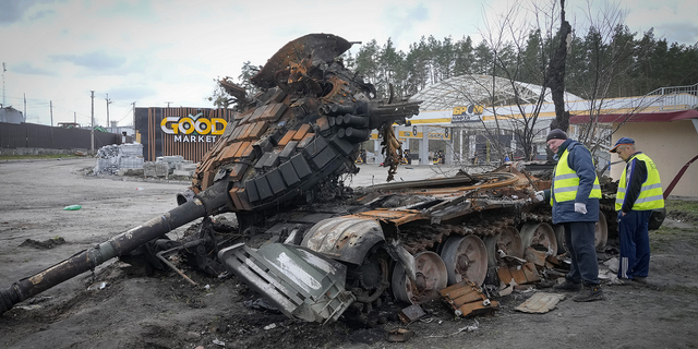Road workers examine a destroyed Russian tank on the highway to Kyiv, Ukraine.