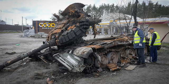 Road workers examine a destroyed Russian tank on the highway to Kyiv, Ukraine.