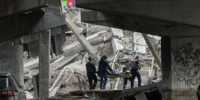 Украинские солдаты несут тело мирного жителя, убитого российскими войсками, под разрушенным мостом в Ирпене под Киевом, Украина, четверг, 31 марта 2022 года.