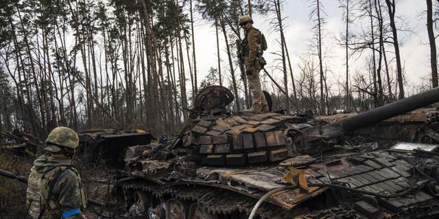A Ukrainian soldier stands on top of a destroyed Russian tank outside Kyiv, Ukraine, Thursday, March 31, 2022. (AP Photo/Rodrigo Abd)