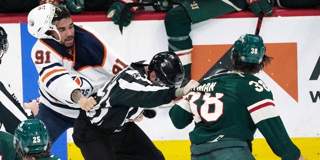 An official, center, gets caught between Edmonton Oilers' Evander Kane (91) and Minnesota Wild's Ryan Hartman (38) during a skirmish in the third period of an NHL hockey game Tuesday, April 12, 2022, in St. Paul, Minn. Both players received game misconduct penalties. The Wild won 5-1, with Hartman scoring two of the goals.