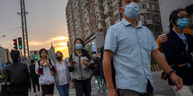 People wearing face masks walk across an intersection during the evening rush hour in Beijing, Wednesday, April 20, 2022. (AP Photo/Mark Schiefelbein)