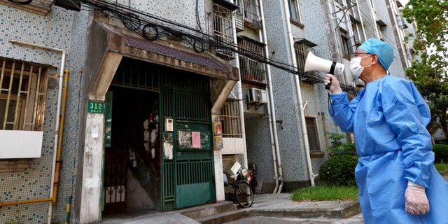 In this photo released by China’s Xinhua News Agency, a volunteer uses a megaphone to talk to residents at an apartment building in Shanghai, China, Tuesday, April 12, 2022. Shanghai has released more than 6,000 more people from medical observation amid a COVID-19 outbreak, the government said Wednesday, but moves to further ease the lockdown on China’s largest city appeared to have stalled. 