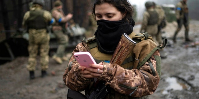 A Ukrainian army soldier, 22, checks her phone after a military sweep to search for possible remnants of Russian troops after their withdrawal from villages in the outskirts of Kyiv, Ukraine, on Friday, April 1, 2022. 