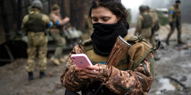 Ukrainian army soldier Dasha, 22, checks her phone after a military sweep to search for possible remnants of Russian troops after their withdrawal from villages in the outskirts of Kyiv, Ukraine, Friday, April 1, 2022.