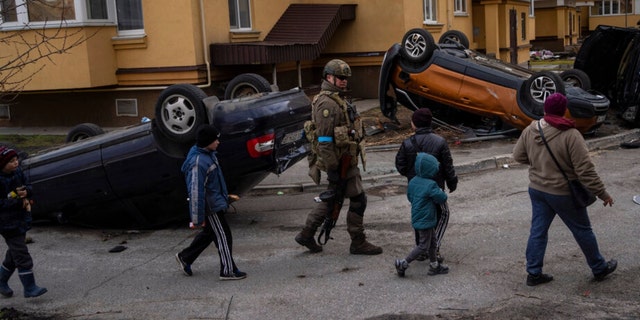A Ukrainian soldier walks with children passing destroyed cars in Bucha, on the outskirts of Kyiv, Ukraine, on Monday.