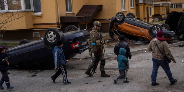 A Ukrainian soldier walks with children passing destroyed cars in Bucha, on the outskirts of Kyiv, Ukraine, on Monday.