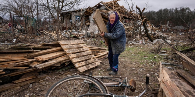 A Ukrainian woman collect wooden planks in a street destroyed by shelling in Chernihiv, Ukraine, on Wednesday, April 13, 2022.