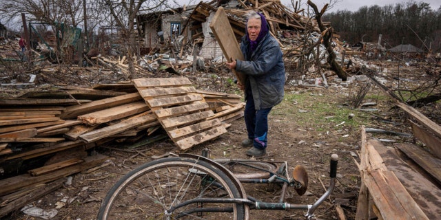 A Ukrainian woman collect wooden planks in a street destroyed by shelling in Chernihiv, Ukraine, on Wednesday, April 13, 2022.