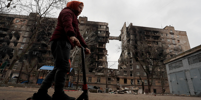 A boy rides a scooter near a destroyed building in Mariupol, Ukraine on Thursday.