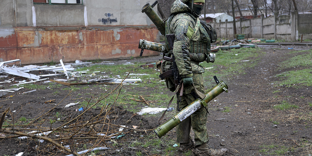 An armed serviceman of Donetsk People's Republic militia walks past a building damaged during fighting in Mariupol on Wednesday<strong>,</strong> April 20.
