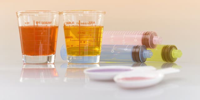 Medicinal cup, oral syringe and teaspoon filled with oral syrup medicine.