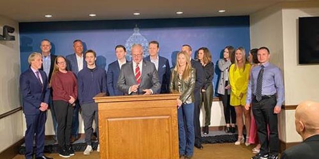 Vince Flynn Day, April 6, is declared in Minnesota; State Rep. Jim Nash is shown delivering remarks at the event on April 6, surrounded by Vince Flynn's family and others.