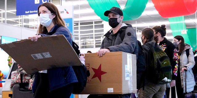 FILE - Travelers line up wearing protective masks indoors at O'Hare International Airport in Chicago, Dec. 28, 2021. (AP Photo/Nam Y. Huh, File)