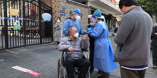 Workers in protective gear help a man in a wheelchair during the mass testing for residents in a lockdown area in the Jingan district of western Shanghai Monday, April 4, 2022. China has sent more than 10,000 health workers from across the country to Shanghai, including 2,000 military medical staff, as it struggles to stamp out a rapidly spreading COVID-19 outbreak in China's largest city. (AP Photo/Chen Si)