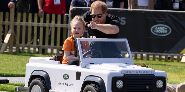 Prințul Harry ajută o fetiță să conducă un mini Land Roar.