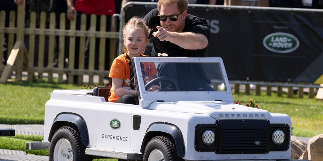 Prințul Harry ajută o fetiță să conducă un mini Land Roar.