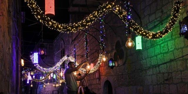 A Palestinian man hangs decorative lights in preparation for the holy Muslim month of Ramadan on the streets of Jerusalem's Old City, Friday, April 1, 2022. 