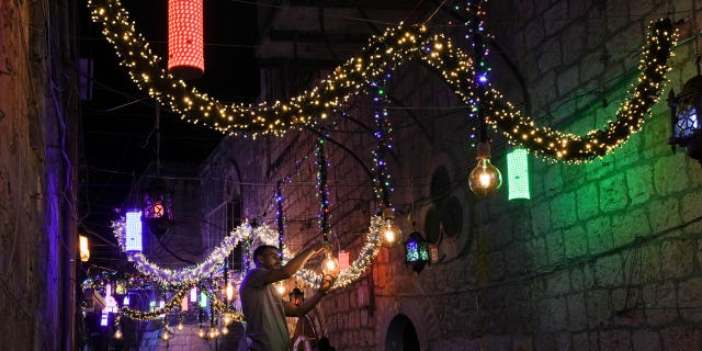 A Palestinian man hangs decorative lights in preparation for the holy Muslim month of Ramadan on the streets of Jerusalem's Old City, Friday, April 1, 2022.