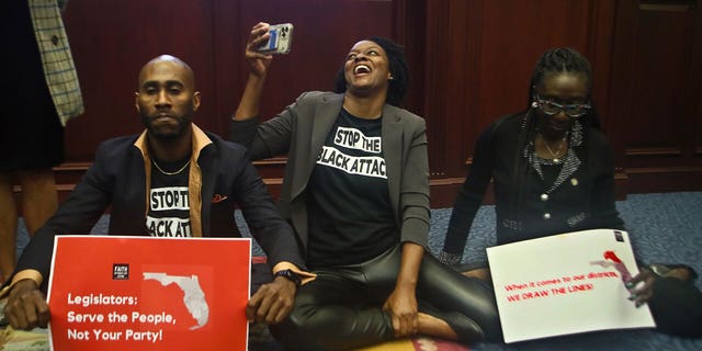 Reps. Tray McCurdy, D-Orlando, Angie Nixon, D-Jacksonville, and Felicia Robinson, D-Miami Gardens, sit on the Florida Seal in protest as debate stops on Senate Bill 2-C: Establishing the Congressional Districts of the State in the House of Representatives on April 21, 2022.
