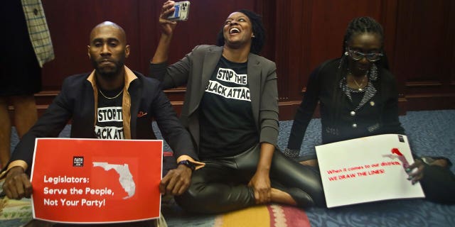 Reps. Tray McCurdy, D-Orlando, Angie Nixon, D-Jacksonville, and Felicia Robinson, D-Miami Gardens, sit on the Florida Seal in protest as debate stops on Senate Bill 2-C: Establishing the Congressional Districts of the State in the House of Representatives on April 21, 2022.