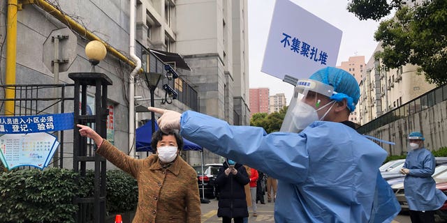 A worker in protective gear holds up a sign which reads "Do not crowd" as he directs a resident near a line for the first round of mass COVID testing in the Jingan district of western Shanghai, China.