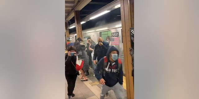 In this photo from social media video, passengers run from a subway car in a station in the Brooklyn borough of New York, Tuesday, April 12, 2022. A gunman filled a rush-hour subway train with smoke and shot multiple people Tuesday, leaving wounded commuters bleeding on a Brooklyn platform as others ran screaming, authorities said. Police were still searching for the suspect. (Will B Wylde via AP)