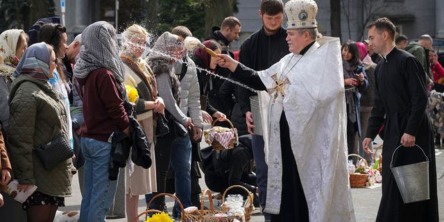 A Ukrainian priest blesses believers as they collect traditional cakes and painted eggs during Easter celebration in Kyiv, Ukraine, Sunday, Apr. 24, 2022.
