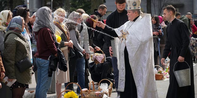 A Ukrainian priest blesses believers as they collect traditional cakes and painted eggs during Easter celebration in Kyiv, Ukraine, Sunday, Apr. 24, 2022.