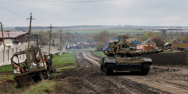 A Ukrainian tank drives next to a destroyed Russian vehicle in the Kharkiv region on April 14.