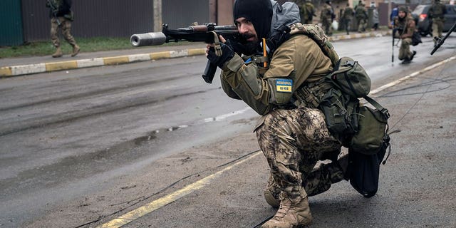A Ukrainian serviceman secures the retreat of fellow soldiers who checked bodies lying on the street for booby traps in the formerly Russian-occupied Kyiv suburb of Bucha, Ukraine, Saturday, April 2, 2022.