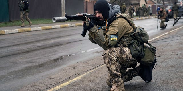 A Ukrainian serviceman secures the retreat of fellow soldiers who checked bodies lying on the street for booby traps in the formerly Russian-occupied Kyiv suburb of Bucha, Ukraine, Saturday, April 2, 2022.