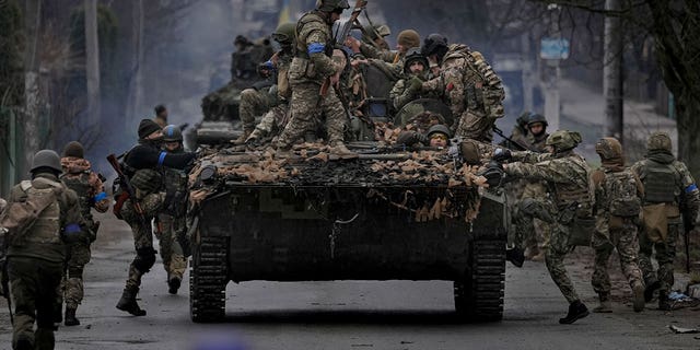 Des militaires ukrainiens grimpent sur un véhicule de combat à l'extérieur de Kiev, en Ukraine, le samedi 2 avril 2022.