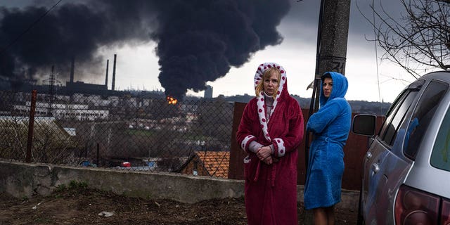After a bombardment in Odesa, Ukraine, on Sunday, April 3, 2022, the woman stays beside the car as smoke rises in the background air. 