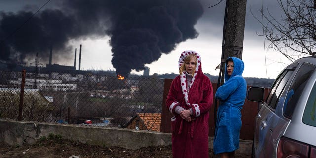 Women stay next to a car as smoke rises in the air in the background after shelling in Odesa, Ukraine, Sunday, April 3, 2022. 