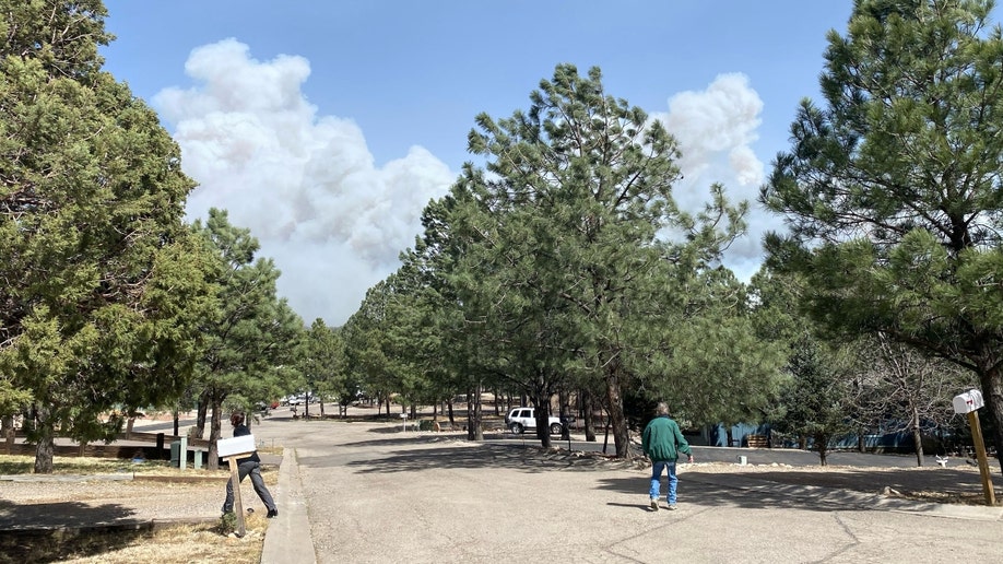 People walk on a street with smoke from New Mexico's McBride Fire rising in the background