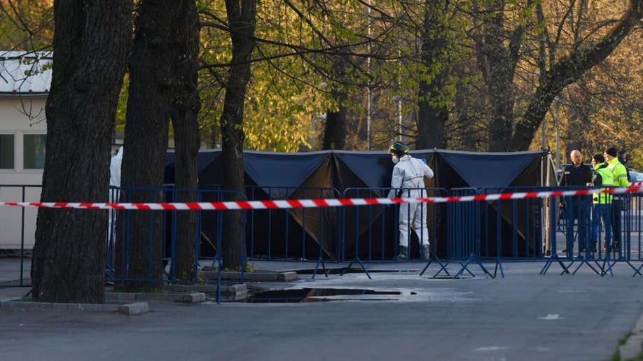 A Romanian serviceman wearing protective gear covers the car that crashed into the gate of the Russian Embassy in Romania.