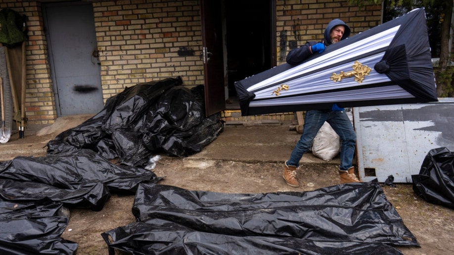 A Ukraine man carries a coffin next to corpses in Bucha
