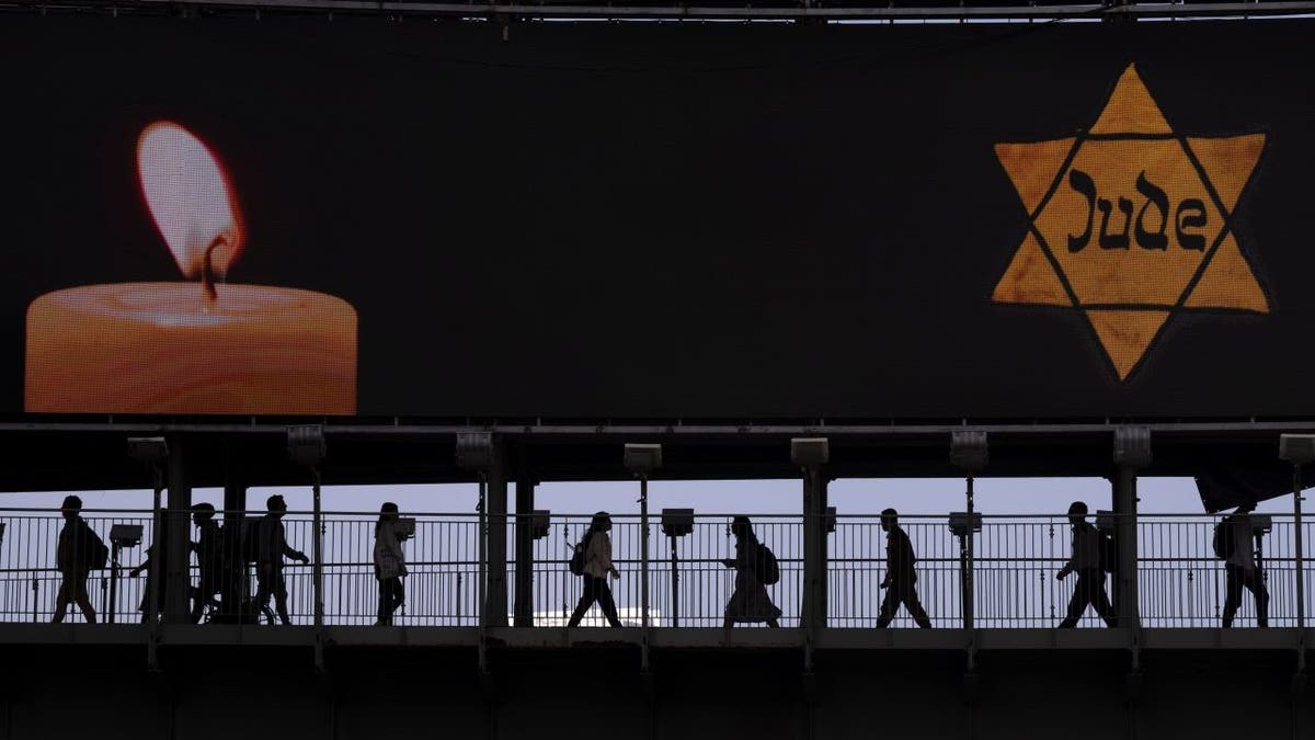 People walk along a bridge under a billboard showing a yellow Star of David, resembling the one Jews were forced to wear in Nazi Germany, on the annual Holocaust Remembrance Day in Ramat Gan, Israel, April 28, 2022.