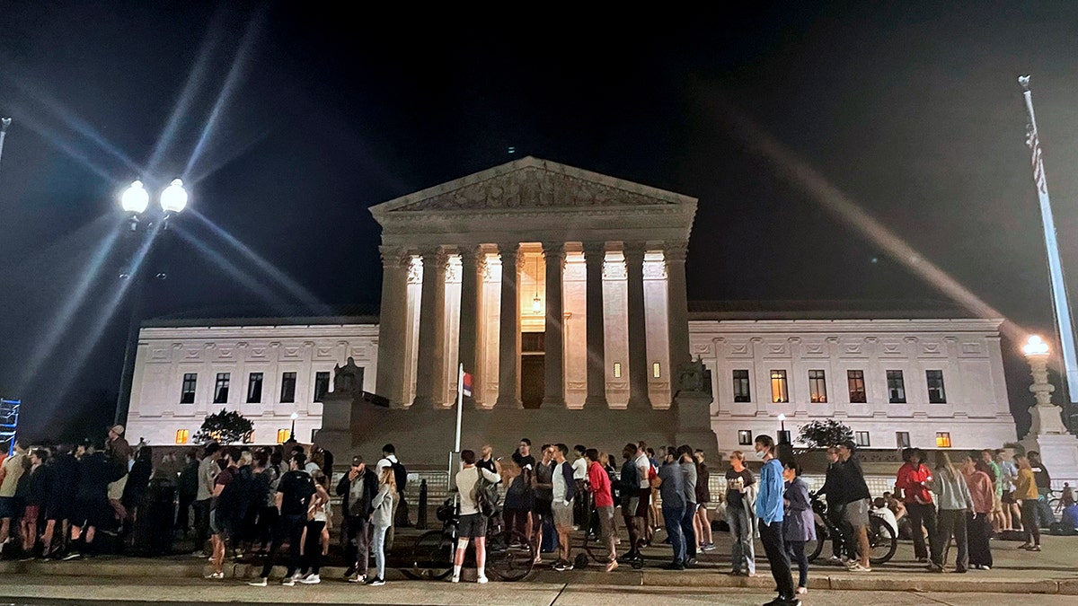 A crowd of people gather outside the Supreme Court, Monday night, May 2, 2022 in Washington.