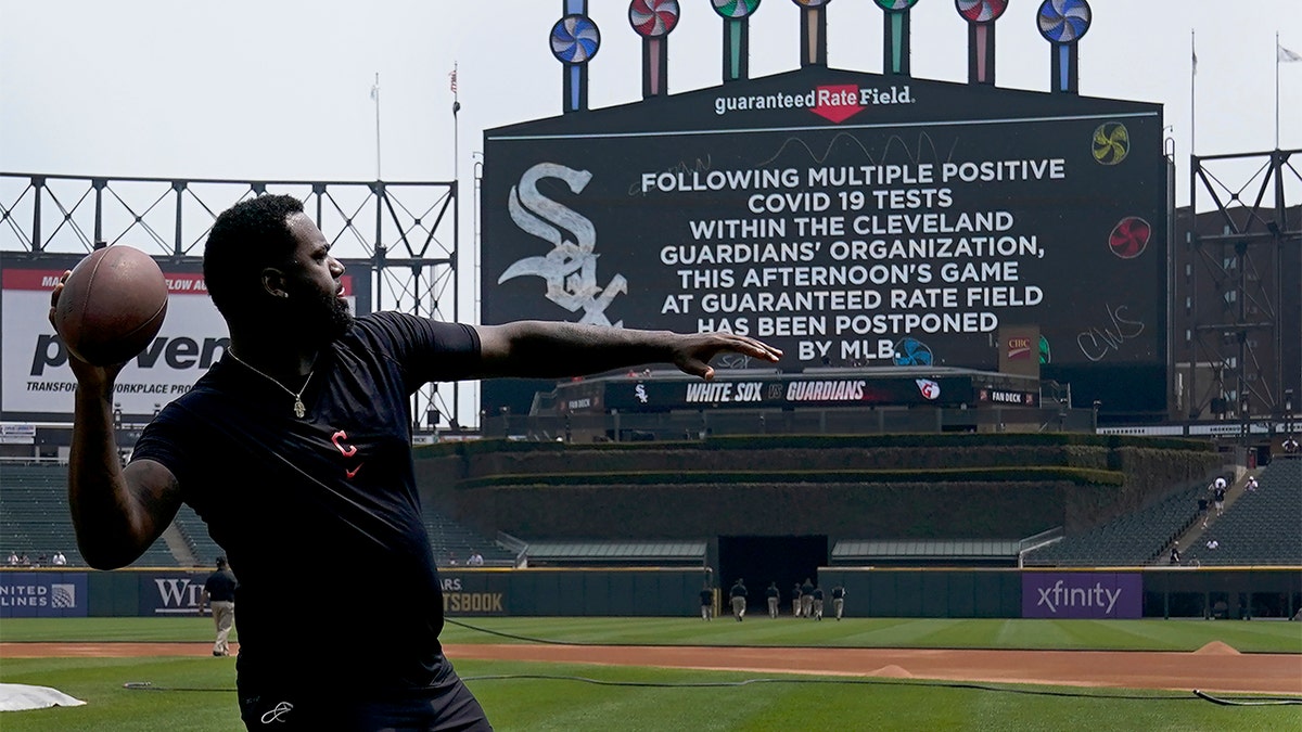 Cleveland Guardians' Franmil Reyes throws a football to teammate Myles Straw as the scoreboard informs fans that the baseball game between the Chicago White Sox and the Guardians has been postponed due to multiple positive COVID-19 tests within the Guardians organization, Wednesday, May 11, 2022, in Chicago.
