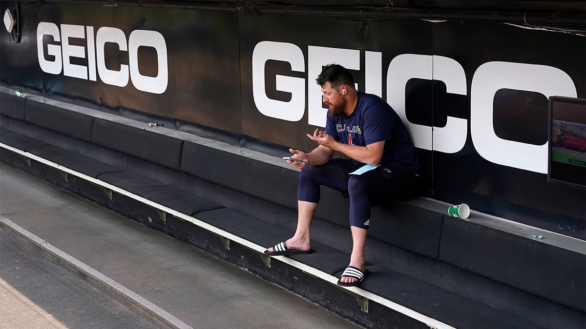 Cleveland Guardians' Bryan Shaw talks on the phone in the dugout after the game between the Chicago White Sox and the Guardians was postponed due to multiple positive COVID-19 tests within the Guardians organization, Wednesday, May 11, 2022, in Chicago.