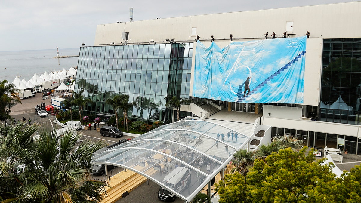Festival workers pull the official poster into place at the Grand Theatre Lumiere during preparations for the 75th international film festival, Cannes, southern France, Sunday, May 15, 2022. The Cannes film festival runs from May 17th until May 28th 2022. (AP Photo/Dejan Jankovic)