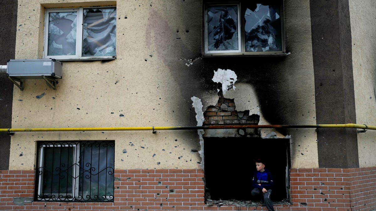 Boy sits in window of destroyed building