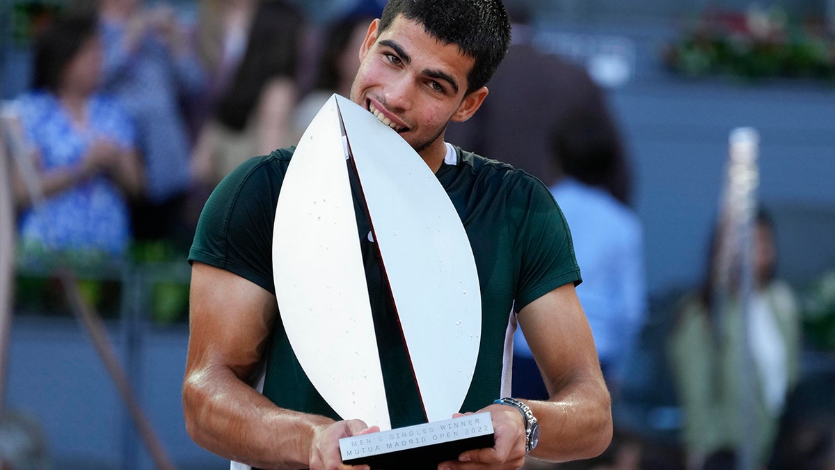 Carlos Alcaraz, of Spain, bites the trophy after winning the final match against Alexander Zverev, of Germany, at the Mutua Madrid Open tennis tournament in Madrid, Spain, Sunday, May 8, 2022. 