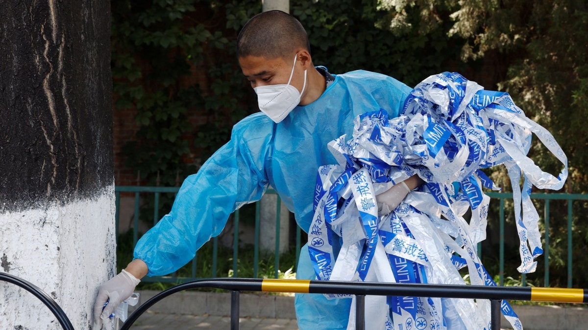 A masked worker in a protective suit removes lines near fences amid a COVID-19 outbreak